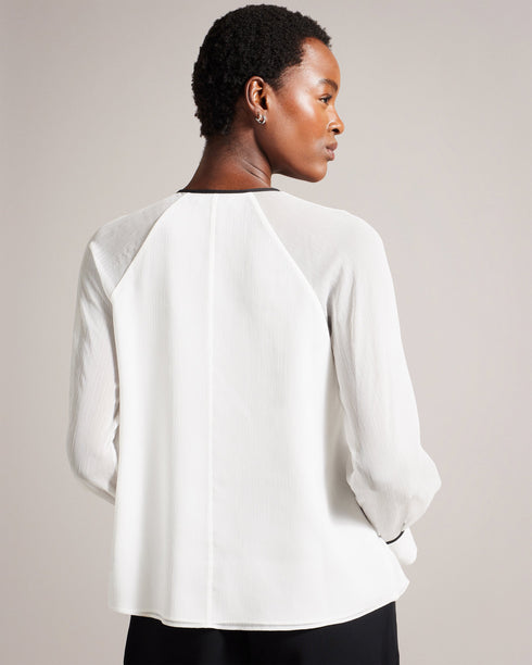 KELEIH-Tops-Channel vintage glamour with a modern twist in the KELEIH blouse. Its delicate organza ruffles and darts exude timeless elegance, while the crew neck keeps it versatile. Whether you're attending a formal event or dressing up for a date night, this blouse will effortlessly elevate your look. Blouse Organza ruffles on front Long sleeves Contrast stitching and neck tie Button fastening Darts on shoulders Crew neck with contrast binding Silvia is 5'11" / 1.8m and wears White in a Ted size 1- Ted Bak